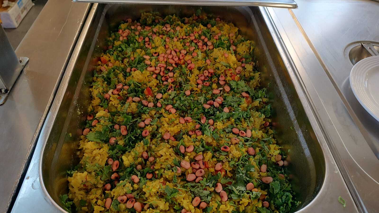 A steel tray of yellow poha topped with roasted peanuts and fresh coriander.