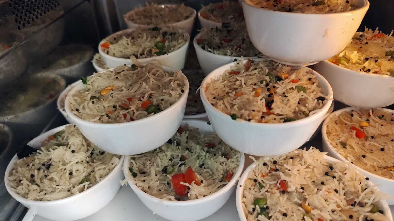 White bowls of vermicelli upma with peas, carrot, peanuts and mustard seeds, stacked in a warmer.